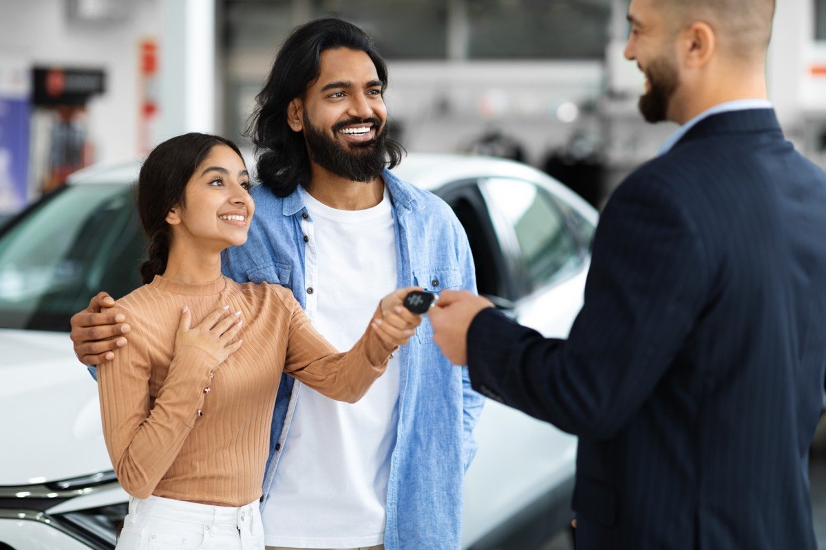 A dealership manager handing car keys to a young Indian family